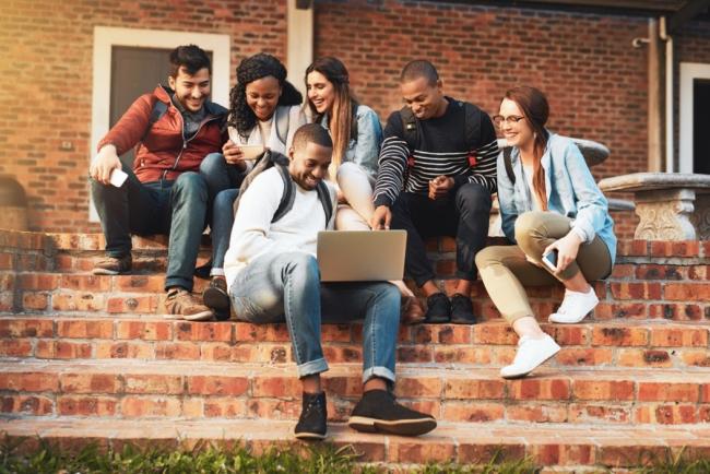 group of diverse students outside watching something on a laptop 